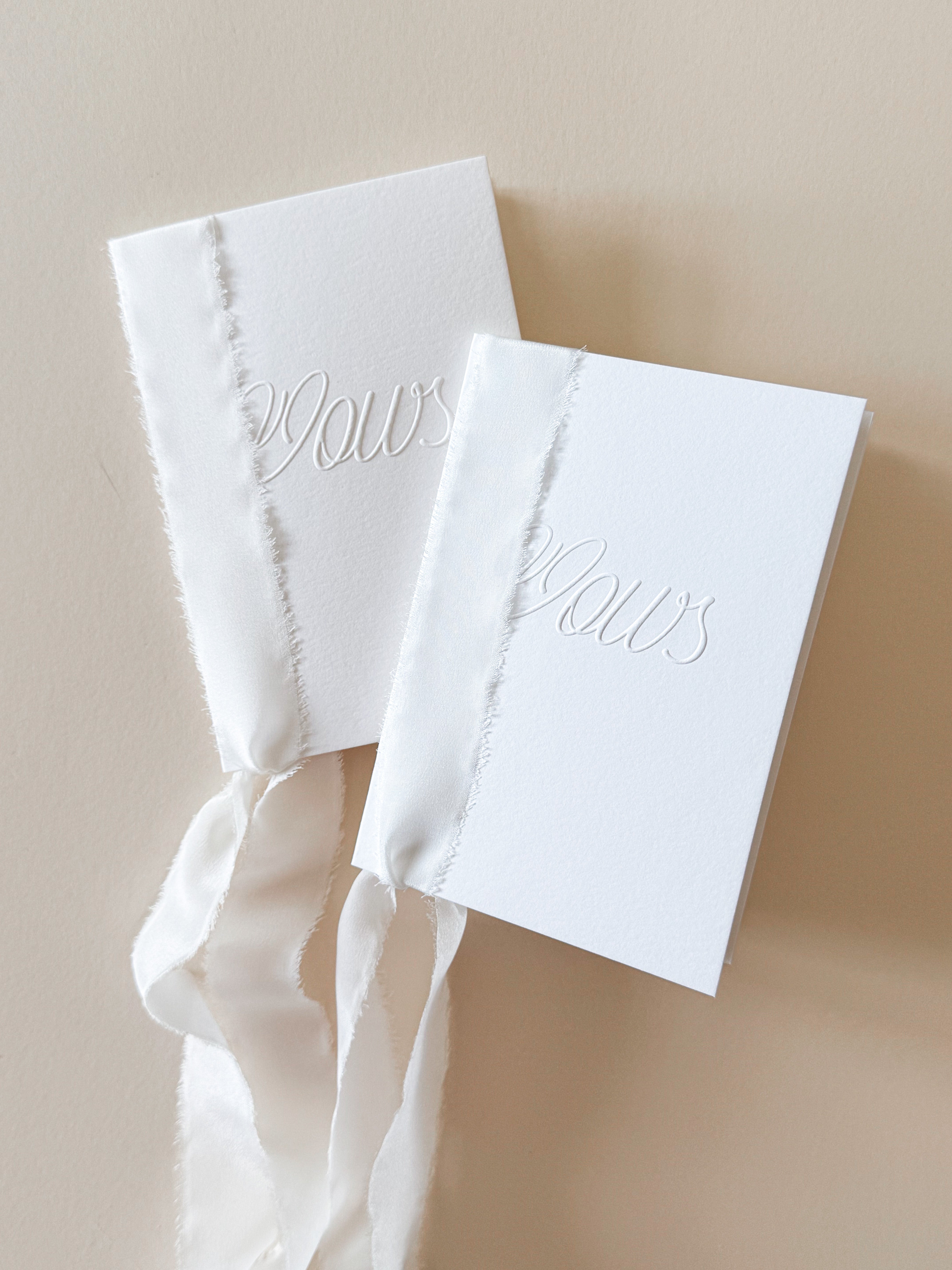 Two white Vow books for wedding ceremonies. Embossed with the word 'Vows' and bound together with white silk ribbon.