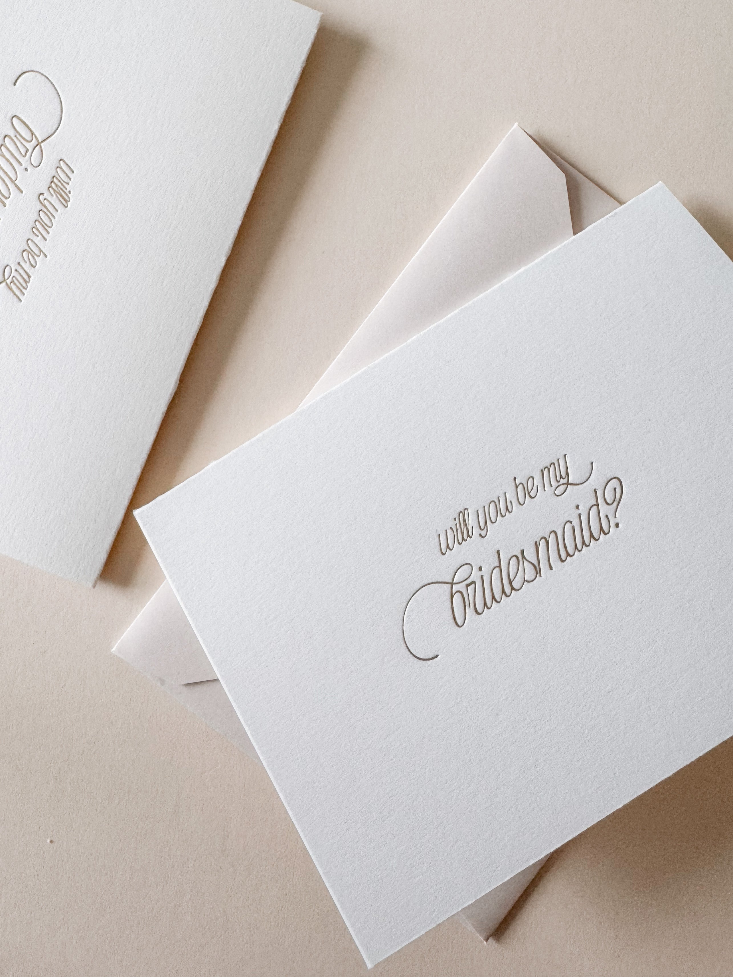 White card with 'will you be my bridesmaid?' text in gold foil with an almond envelope