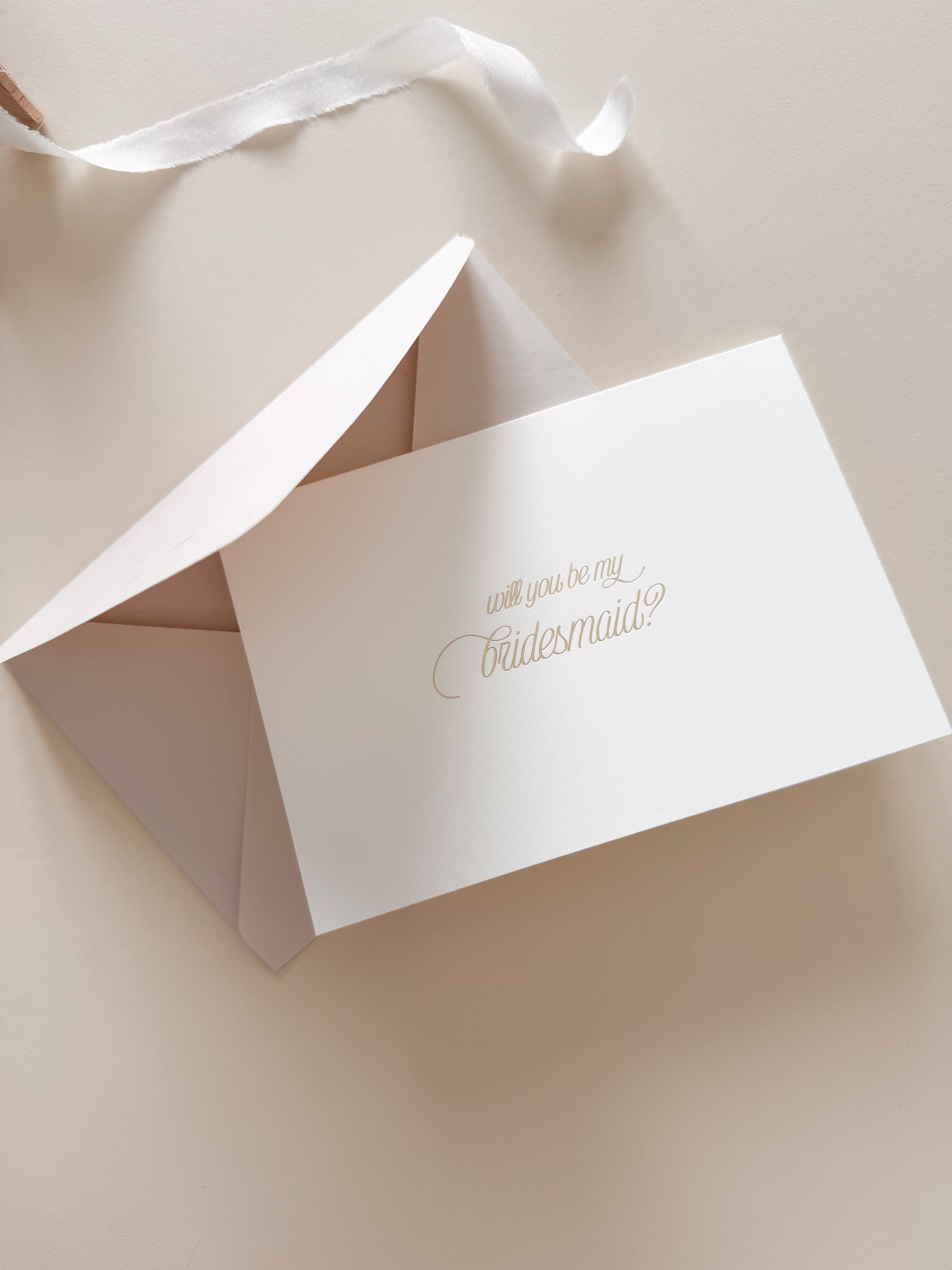 A hand-stamped bridesmaid proposal card with gold foil on a warm white background, the card is blank inside and a premium Almond coloured envelope is included.