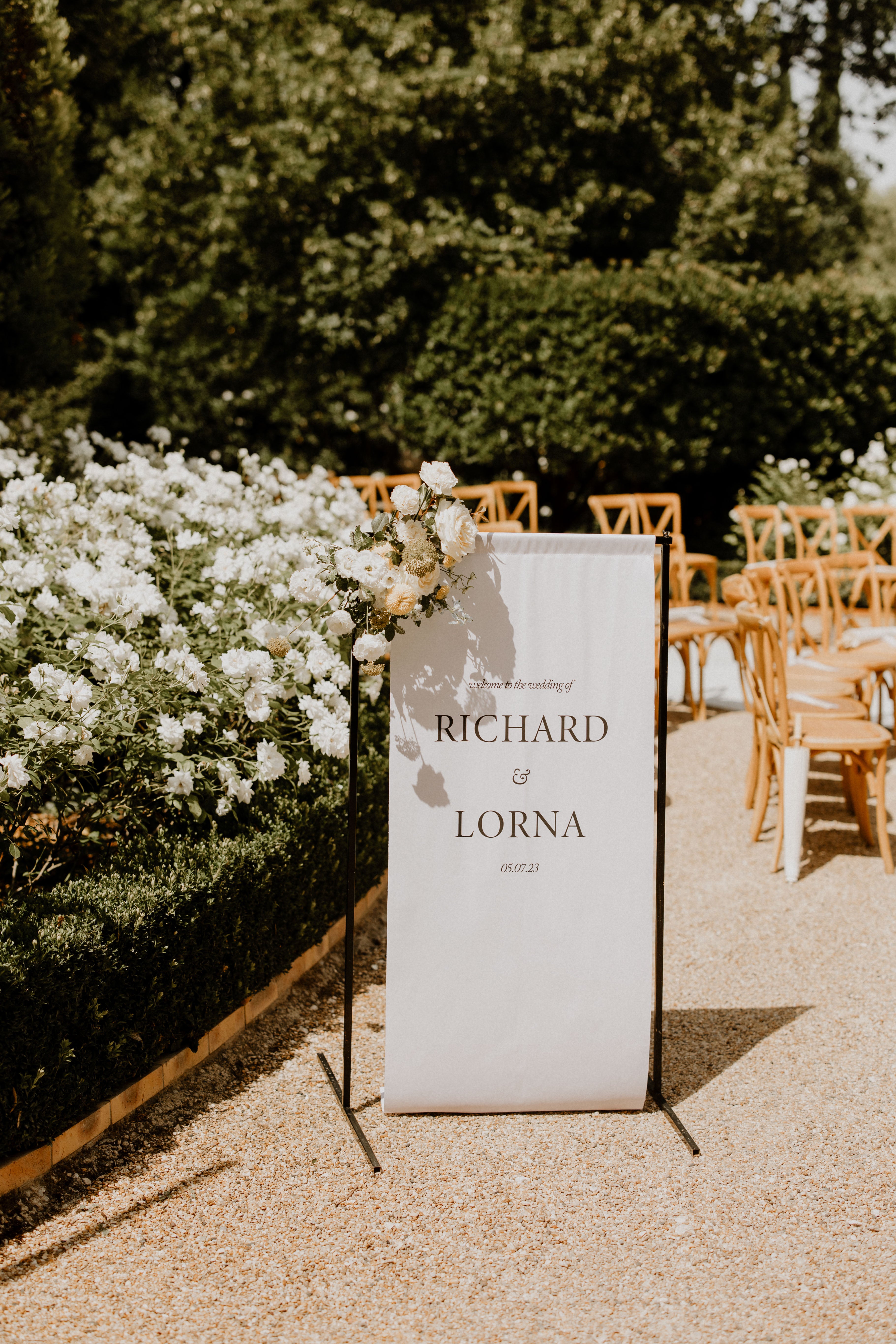 Welcome sign by Lavender Muse at an outside wedding in Provence, linen banner on black stand with florals