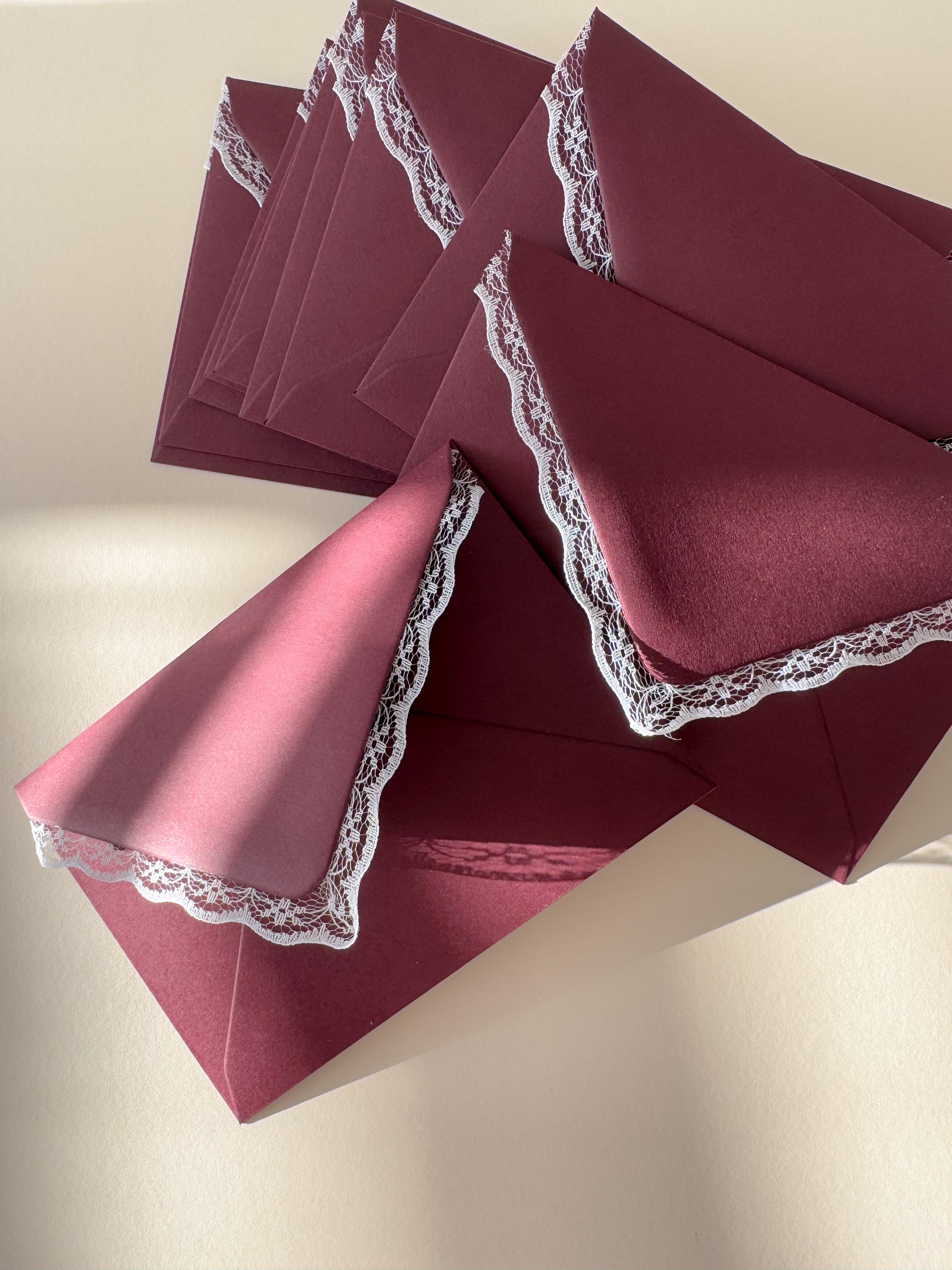 Stack of vintage Inspired burgundy envelopes with lace trim sat in the sunlight