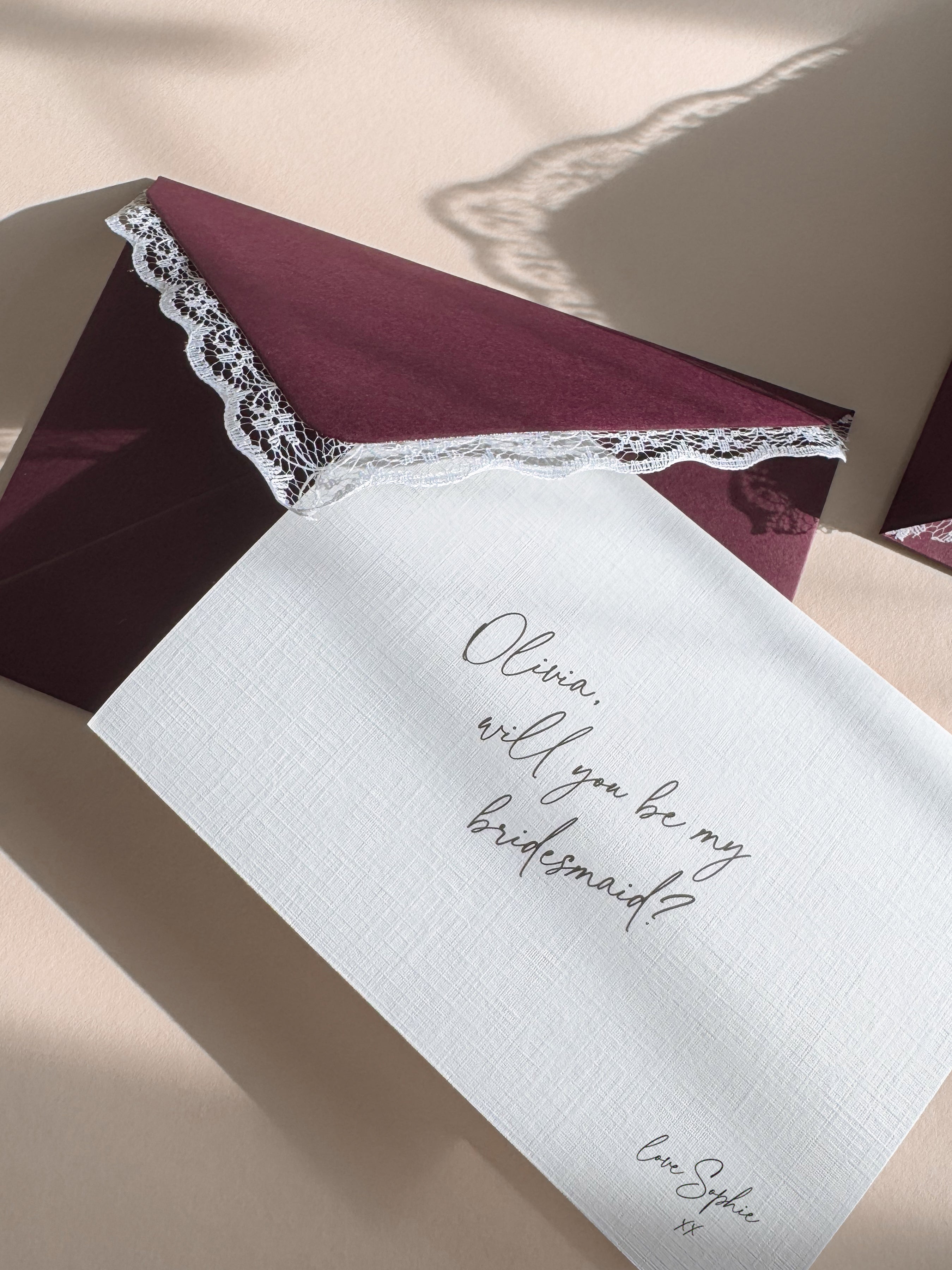 Vintage Inspired Burgundy Envelope with Lace Trim pairs with a personalised bridesmaid proposal card on linen textured cardstock and handwritten script font.
