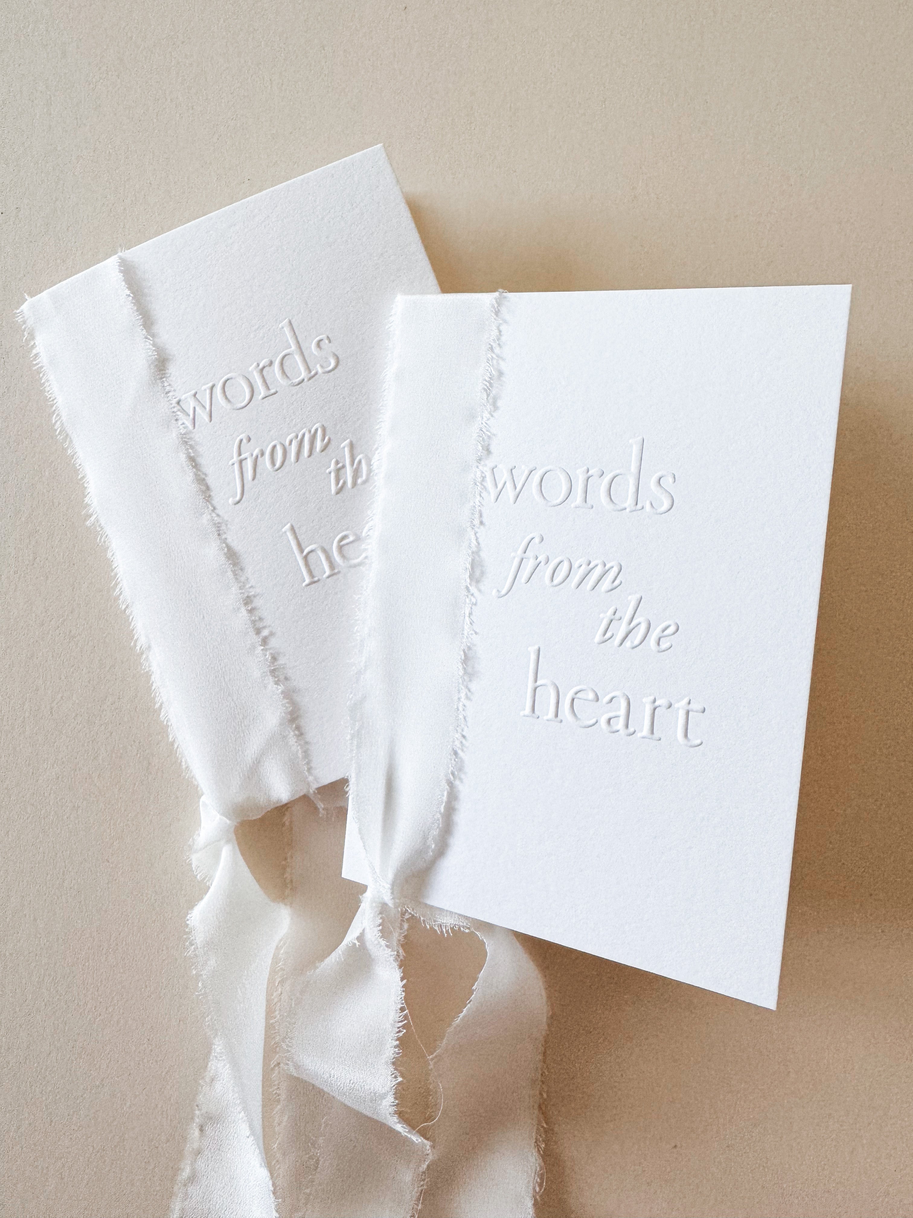 Two white card speech books with 'words from the heart' text embossed on the front, bound together with white silk ribbon.